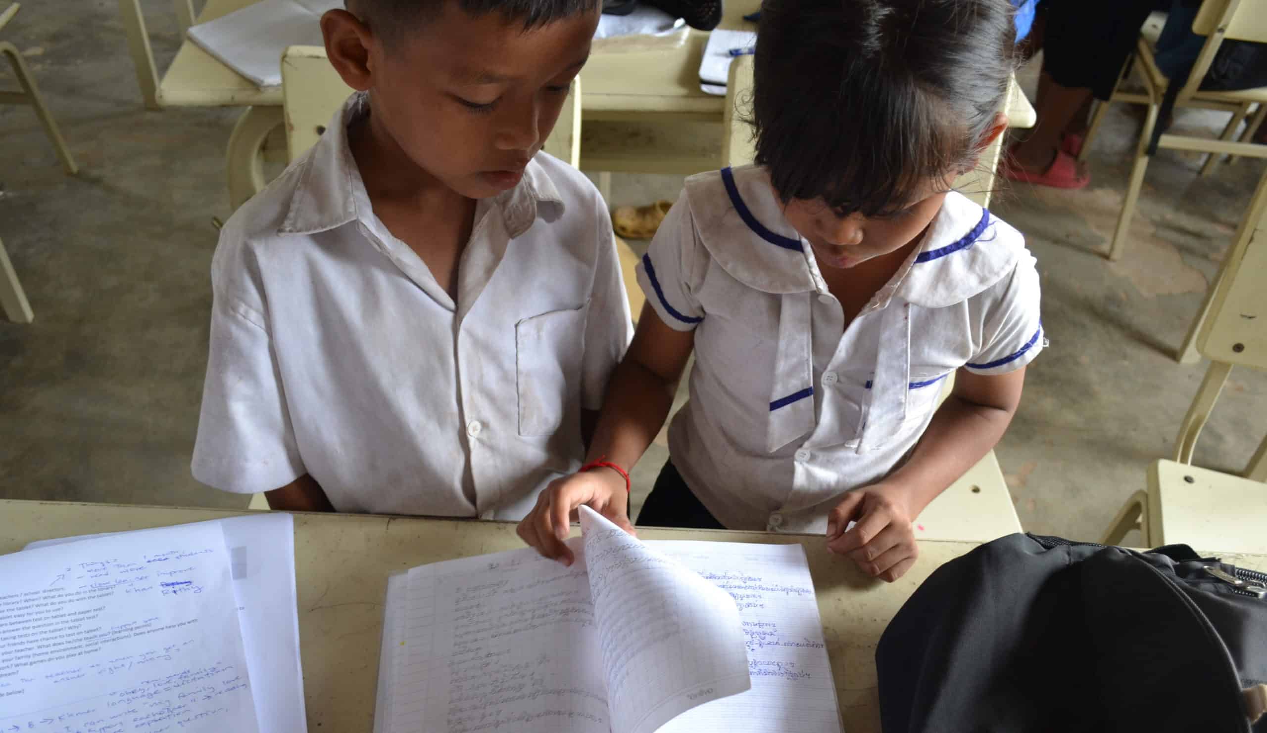 Two Cambodian school children look over their notes from class while sitting at a desk.