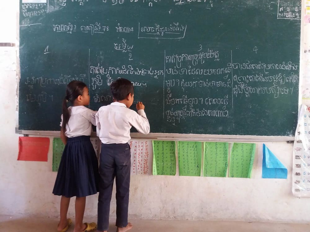 Two young cambodian students work on a problem on a chalkboard.