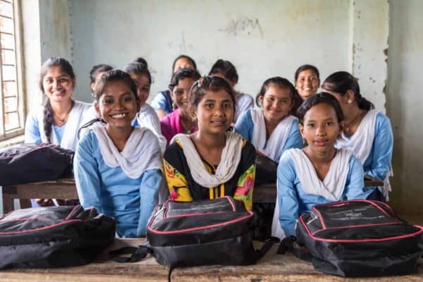 Nepali school girls sit at their desks in a classroom smiling.