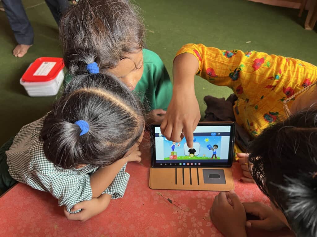 3 young children play learning games on a tablet around a table