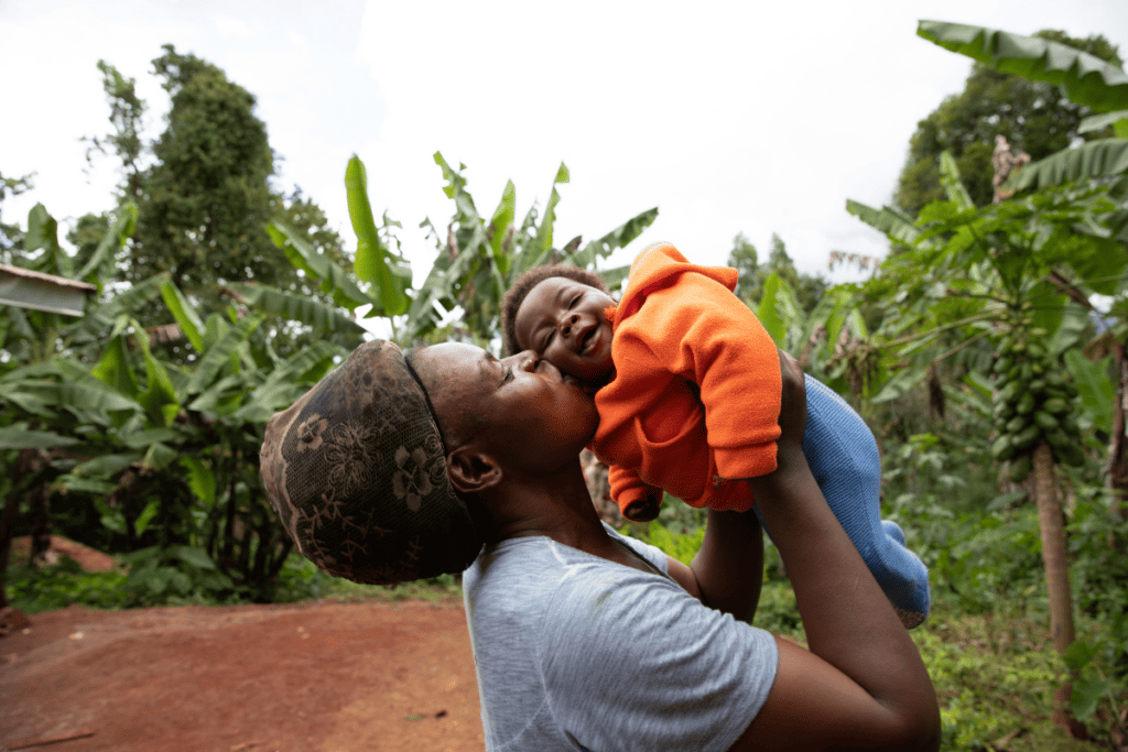 African mother holds and kisses young baby outdoors