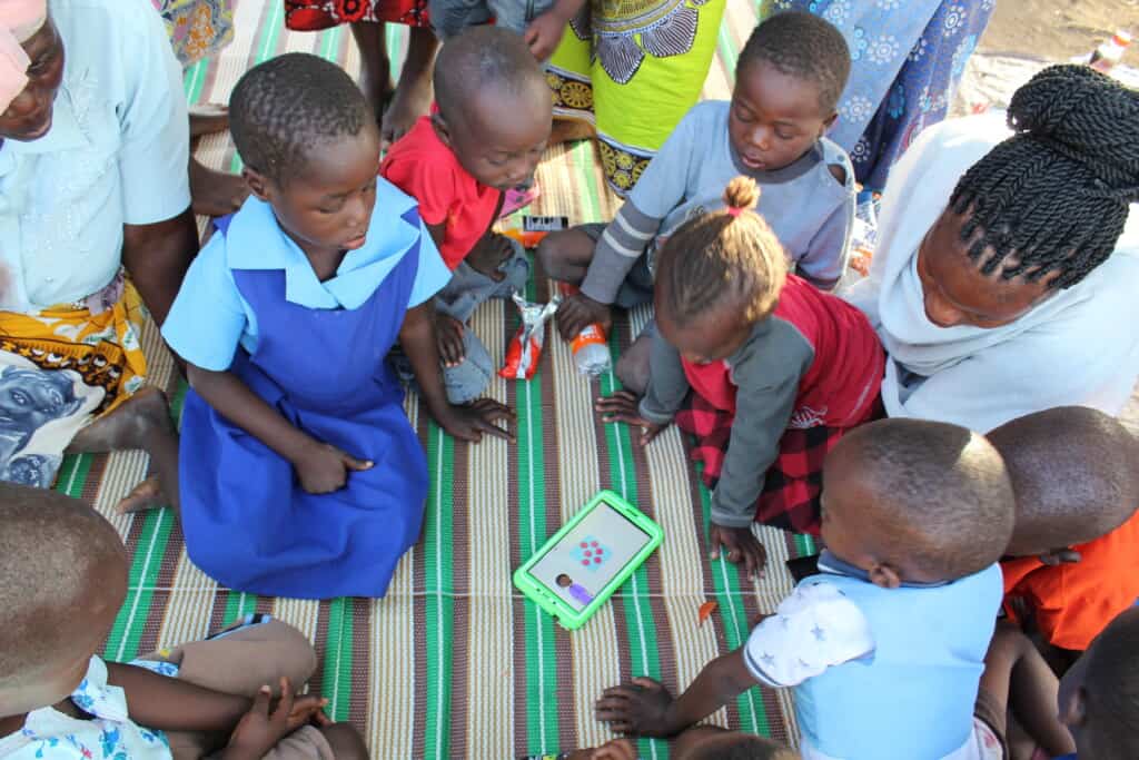 Young kids and parents sit around a tablet in Malawi
