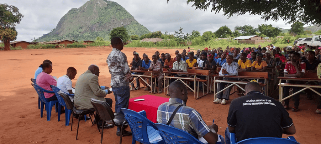 A community gathering in northern Mozambique where leaders sit at the front in a line of chairs and community members sit across in at tables