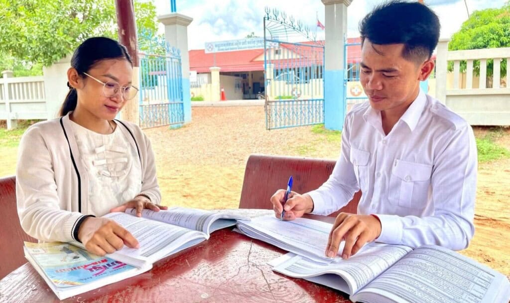 A mentor works with a teacher at an outside table in Cambodia