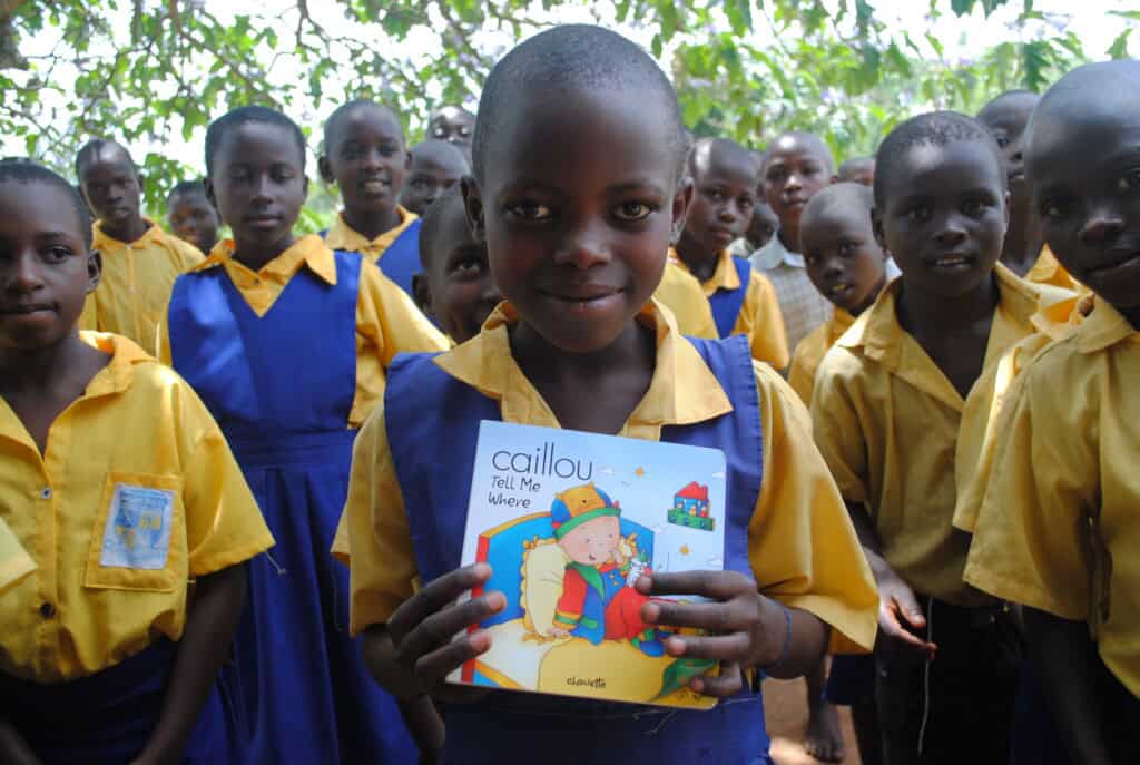 a young student in Uganda holds a book at the front of a group of students in uniform