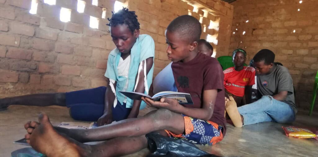 Two students sit on the floor of a classroom reading books in Mozambique